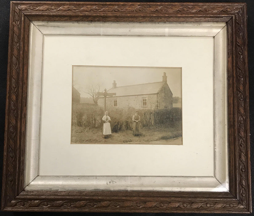 Antique photo of two people in front of a house in a carved wooden frame 