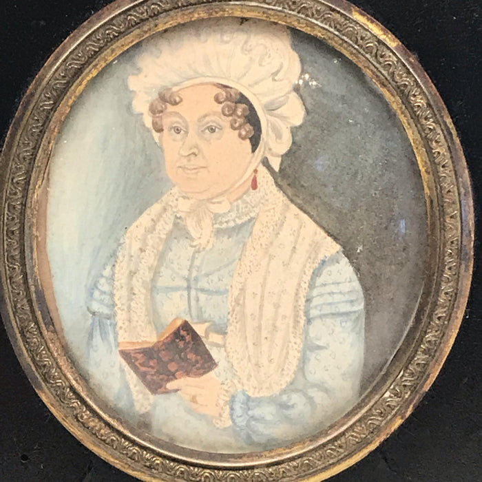 Antique painting of a women reading in a black frame with gold detailing 