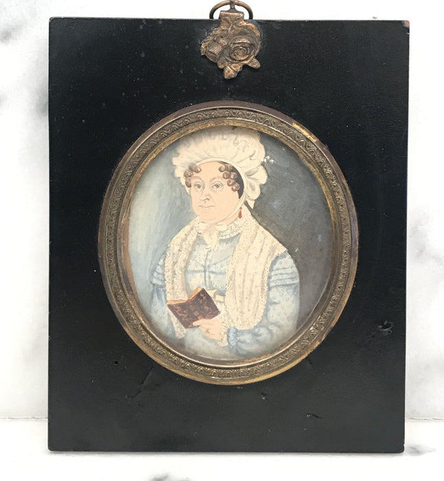 Antique painting of a women reading in a black frame with gold detailing 