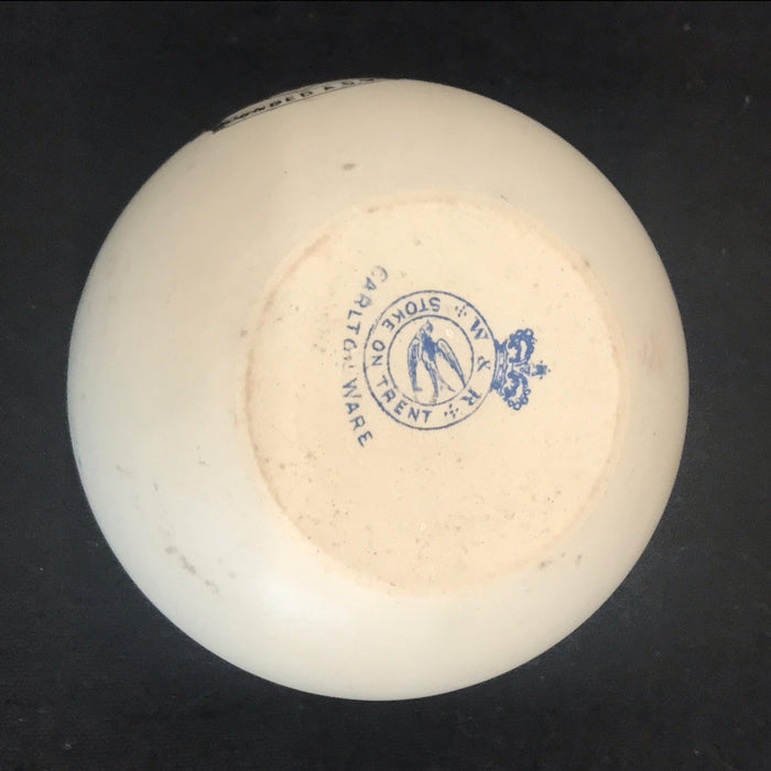 Antique white round match striker with a red coat of arms design on the front